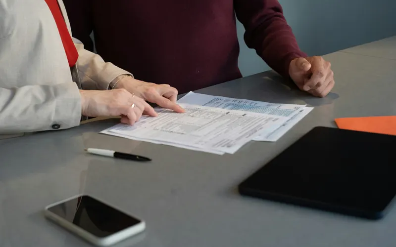 Dos personas repasan unos impresos sobre la mesa, junto a un móvil y una tableta